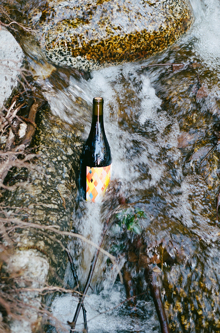 A bottle of Martha Stoumen Benchlands 2022 sitting upright on a rock in a rushing creek.