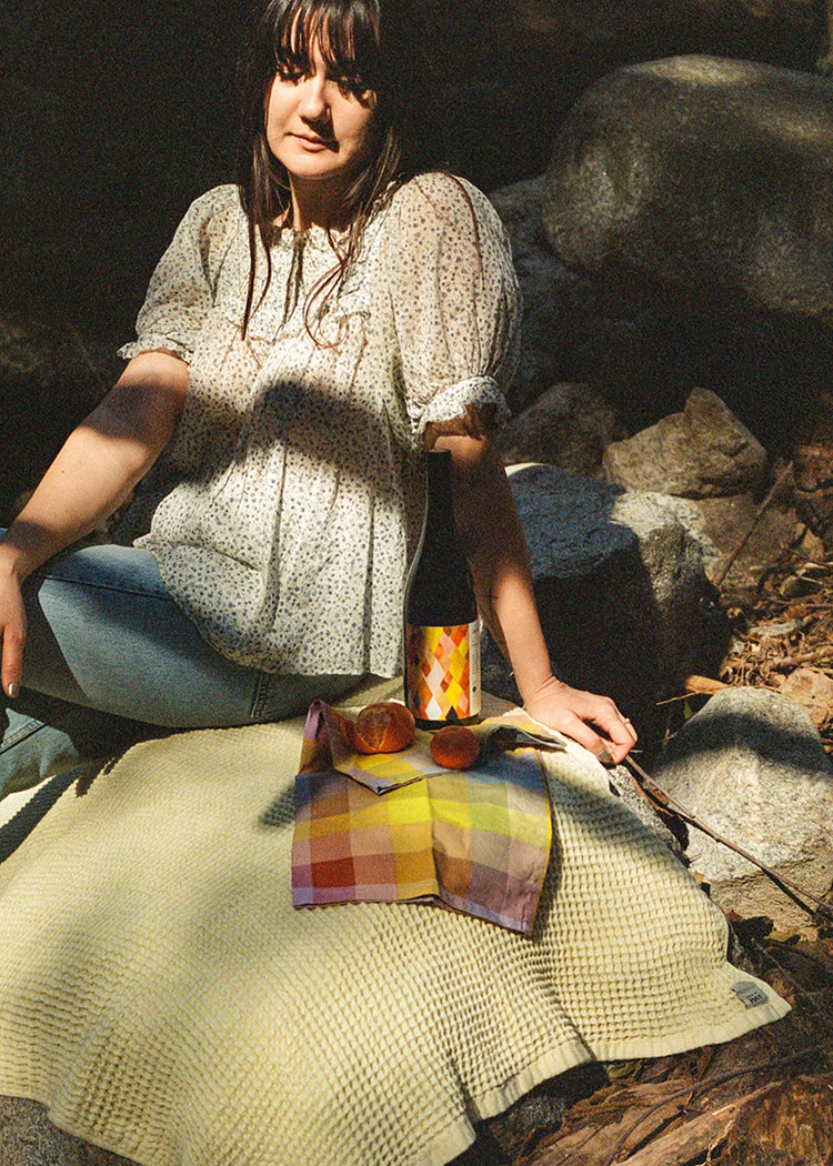 A woman sits on a beach towel with a bottle of Martha Stoumen Benchlands and tangerines.